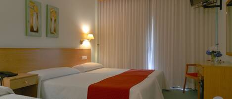 A hotel room with two beds, a desk, a chair, a TV mounted on the wall, and a window with curtains.