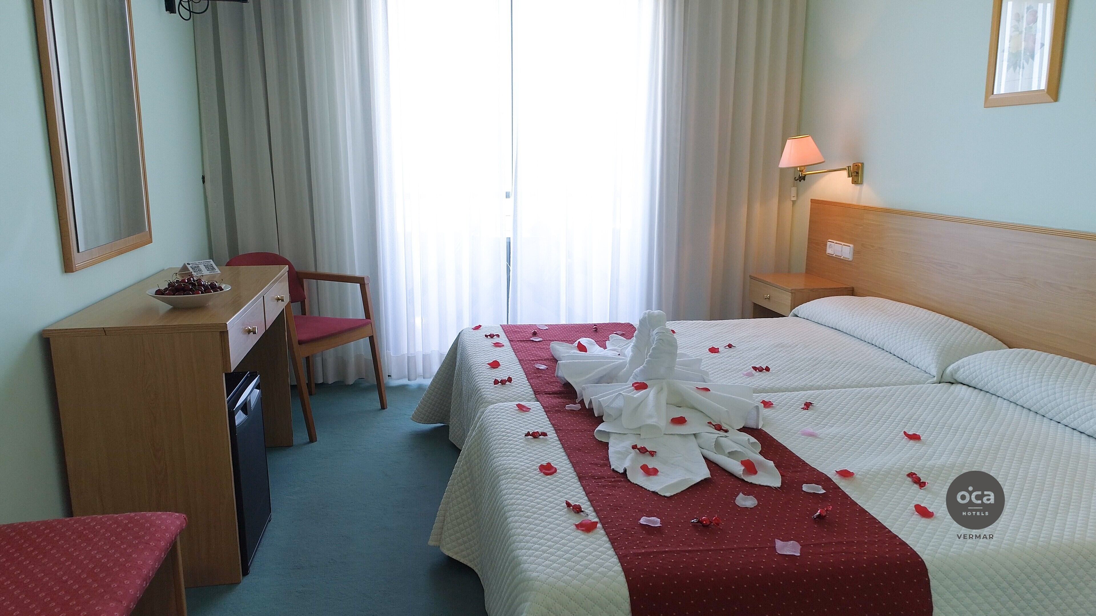 Une chambre d’hôtel avec un lit, un bureau, une chaise, une table de chevet et une lampe.