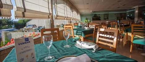 Comedor de hotel con mesas dispuestas para dos, con manteles verdes y sillas de madera.