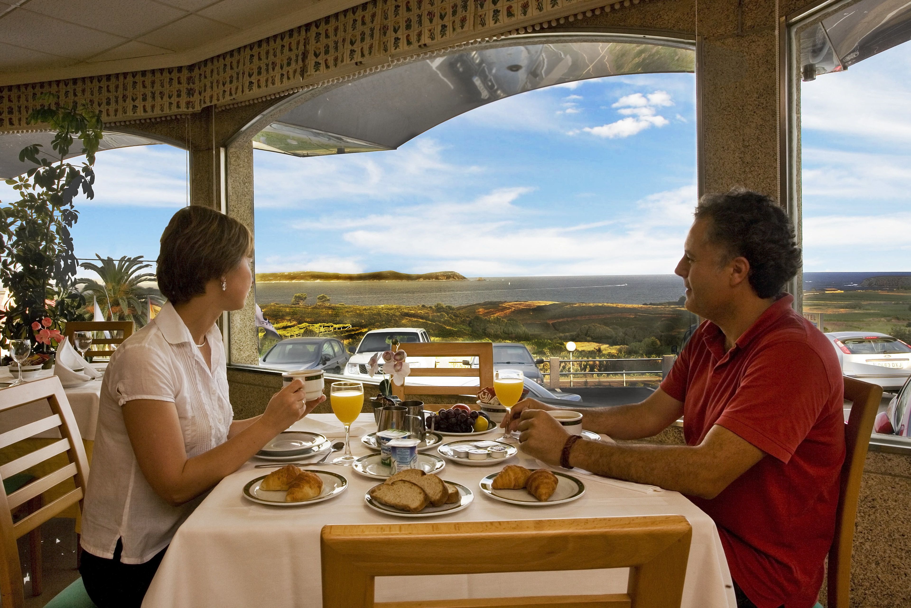 A dining table with plates of food, a glass of orange juice, and a view of the sea.