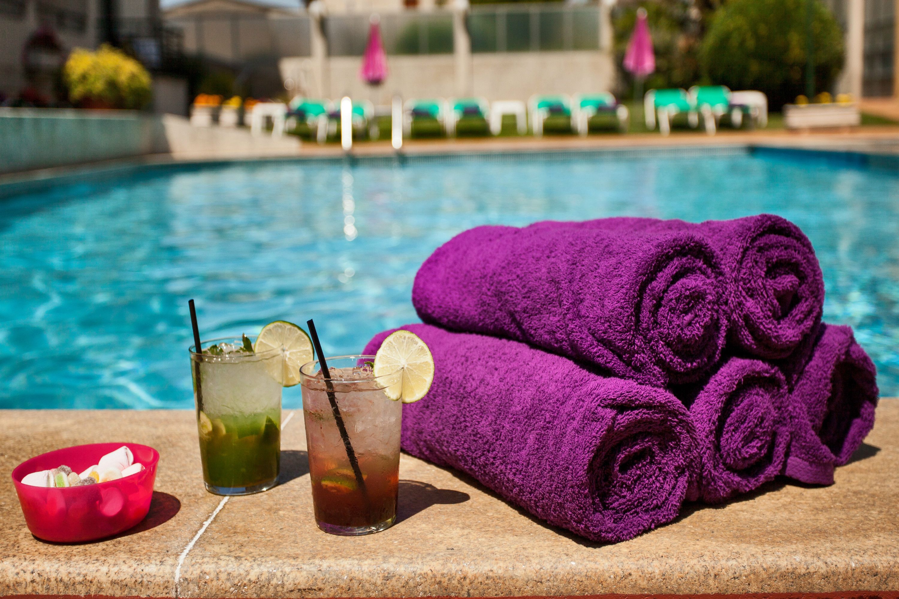 A poolside setting with a drink, a bowl, and rolled towels.