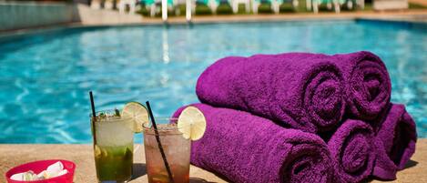 A poolside setting with a drink, a bowl, and rolled towels.