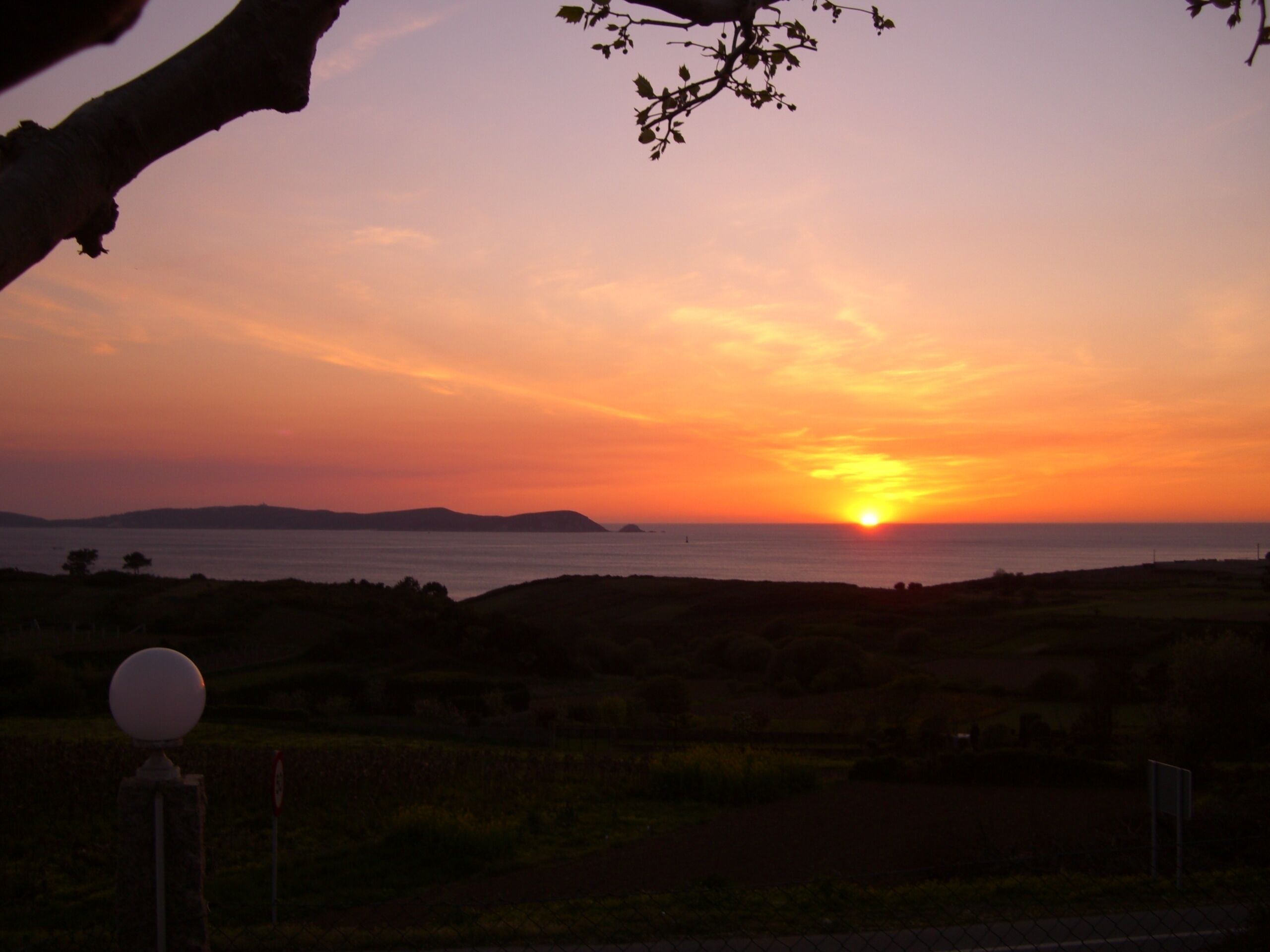 A sunset over a coastal landscape with rolling hills and a body of water.