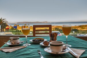 Una mesa servida con alimentos y bebidas para el desayuno, con vistas a un paisaje costero.