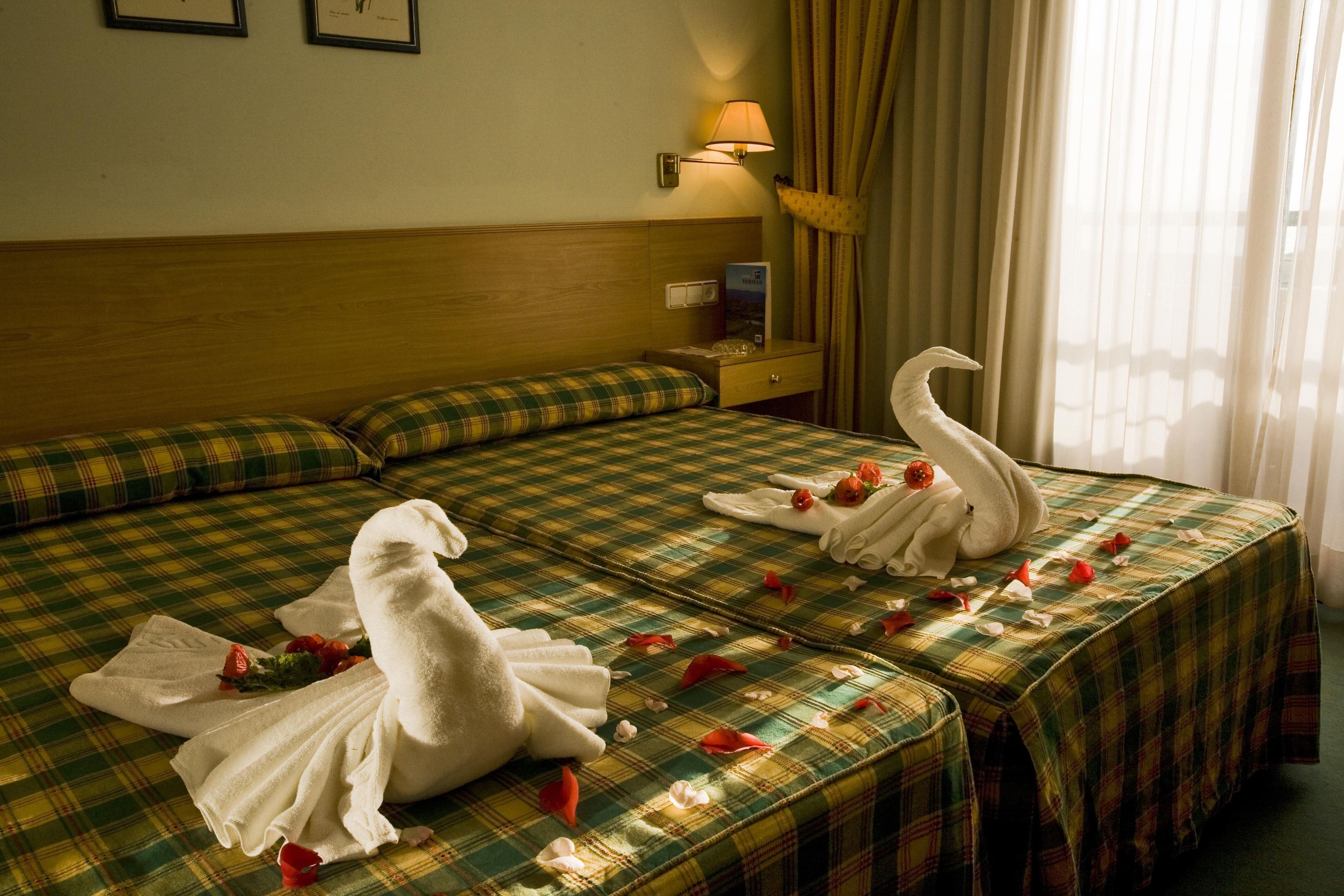 A hotel room with a bed covered in a plaid bedspread, a bedside lamp, and a decorative swan towel arrangement.