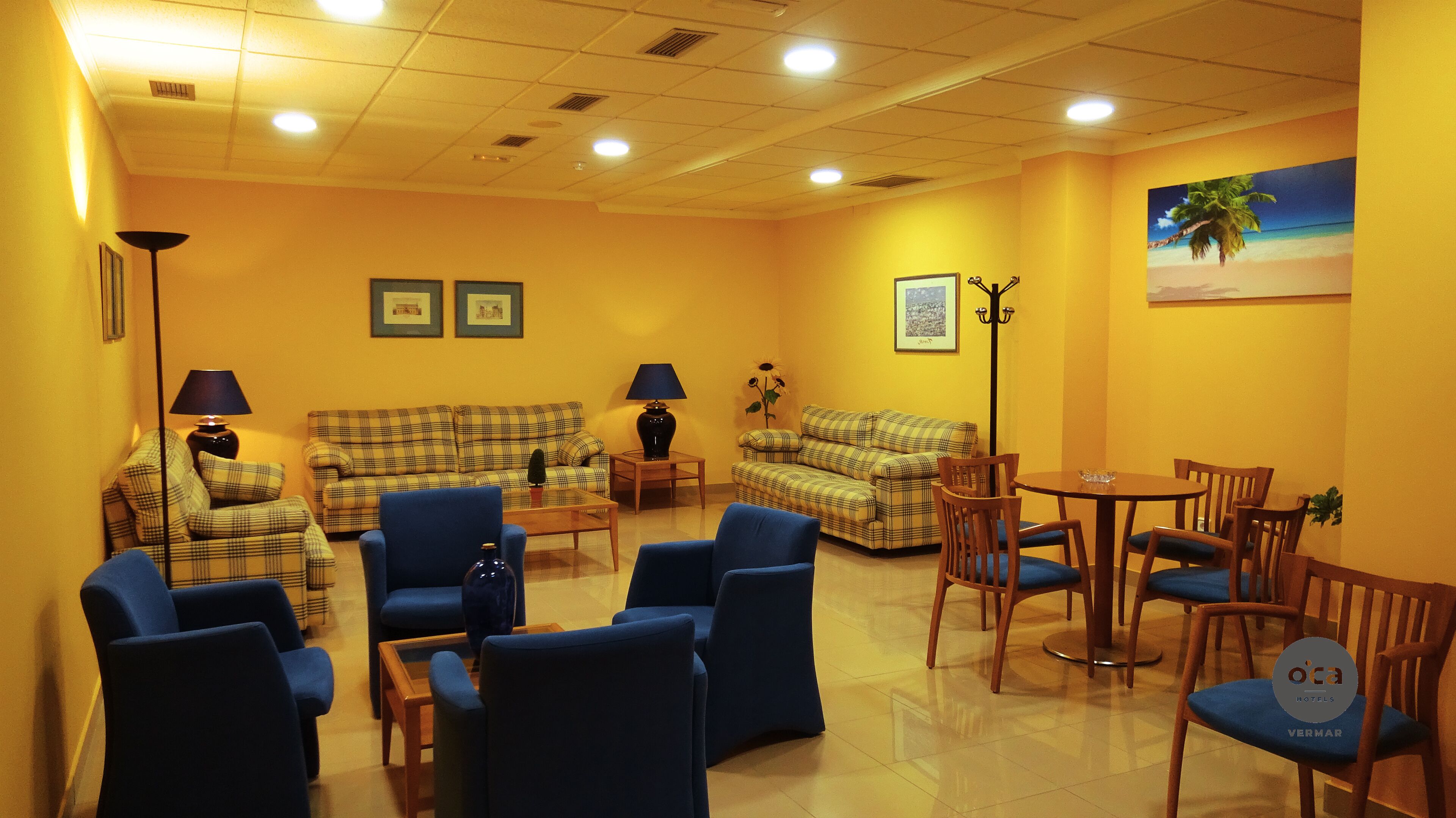 Una camera d'albergo dal tema giallo, con due divani, diverse poltrone, un tavolino e un quadro raffigurante una spiaggia.