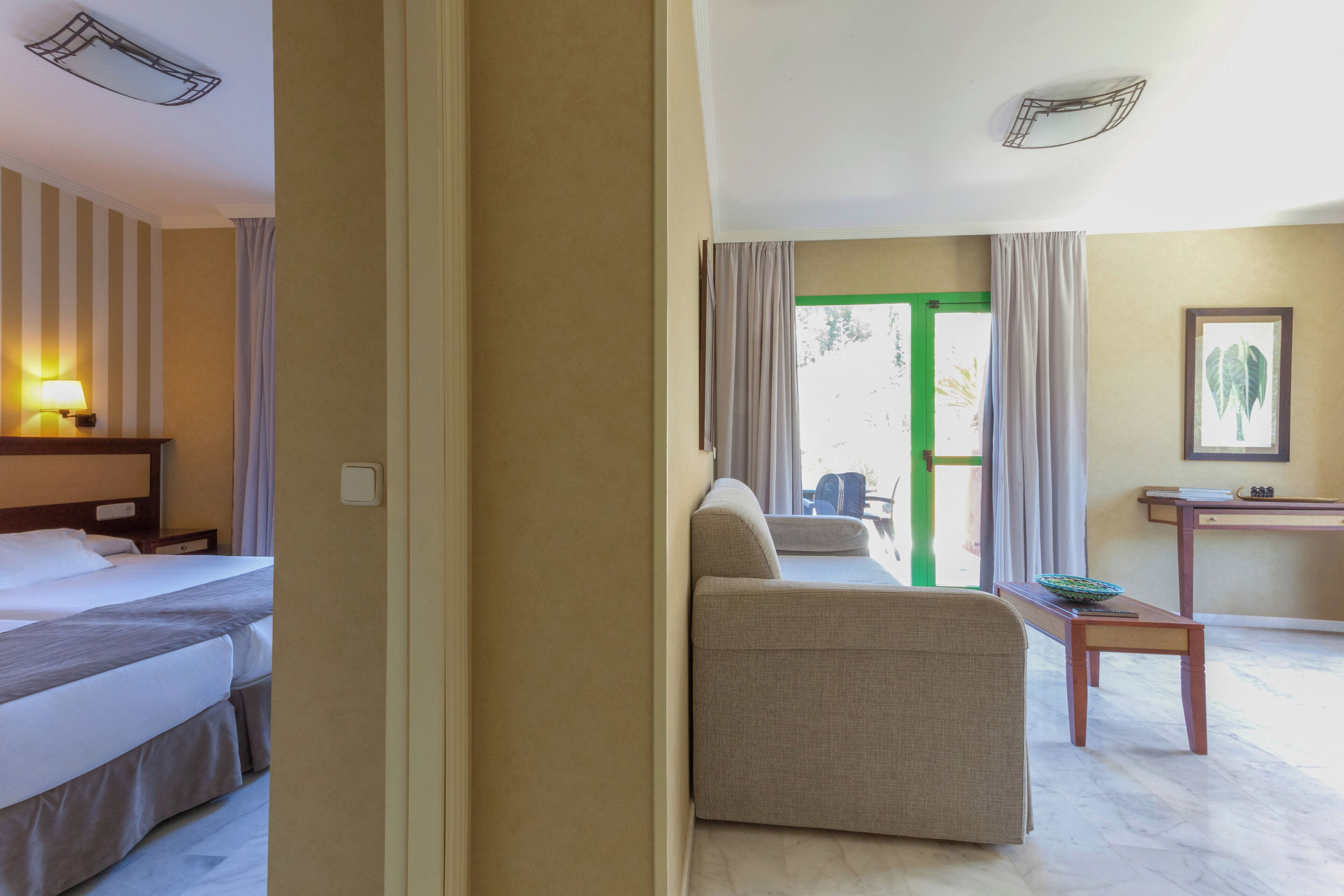 A hotel room with a bed, a sofa, a small table, and a view of the outdoors.