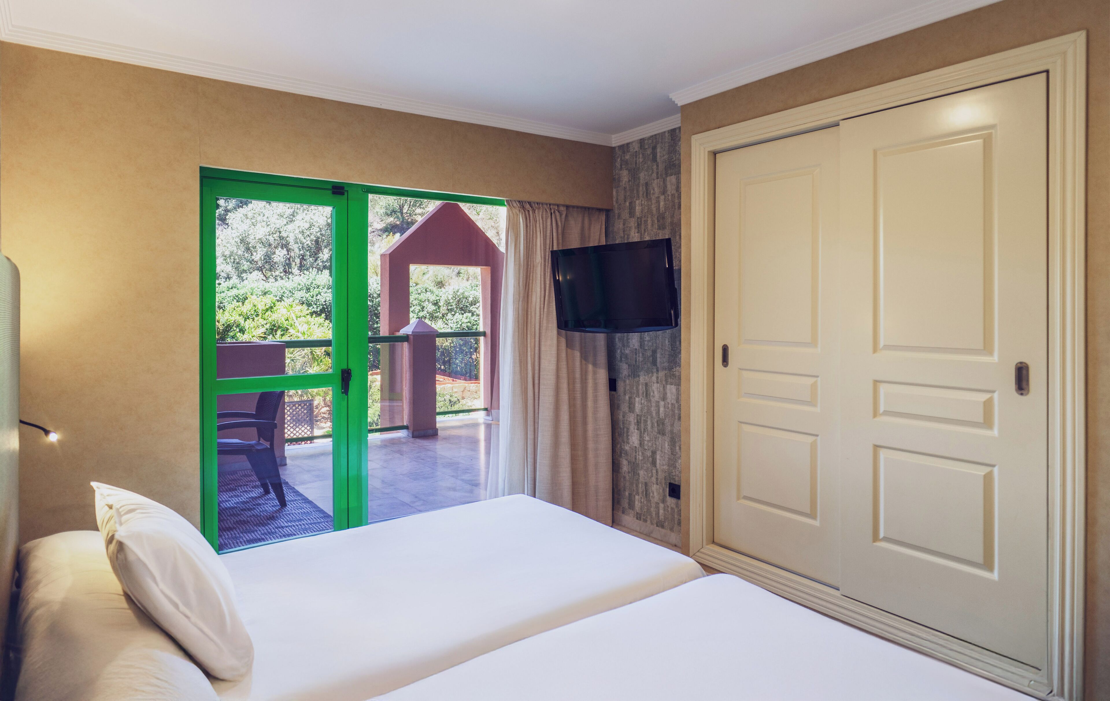 Une chambre d’hôtel équipée d’un lit, d’un téléviseur fixé au mur et d’une porte-fenêtre coulissante donnant sur un espace extérieur.