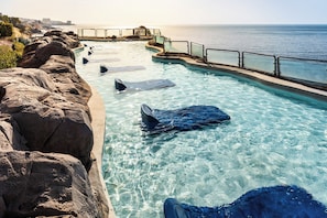 A clear pool with sharks swimming, surrounded by rocks and a view of the ocean. - Holiday World Riwo, Affiliated by Meliá (Benalmádena)
