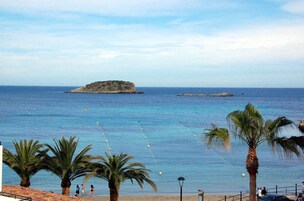 Una playa con palmeras, un afloramiento rocoso y un mar azul cristalino.