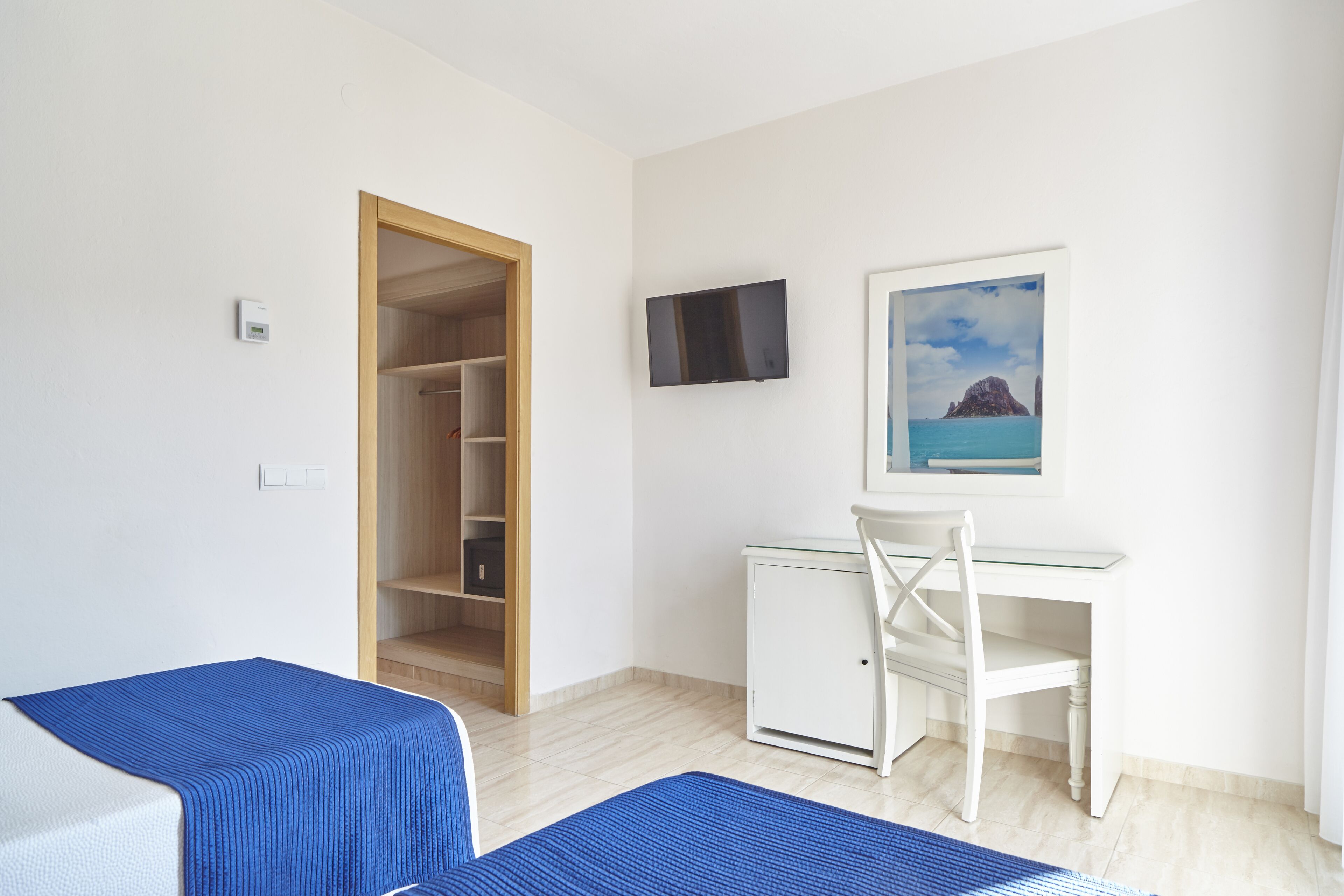 Una habitación con cama, escritorio, silla, televisor y un cuadro.