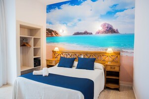 Un dormitorio con una cama, mesitas de noche de madera, un armario y un mural de playa en la pared.