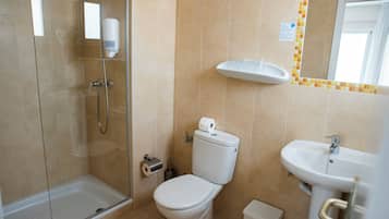 A bathroom with a glass shower enclosure, a toilet, a sink, and a mirror.