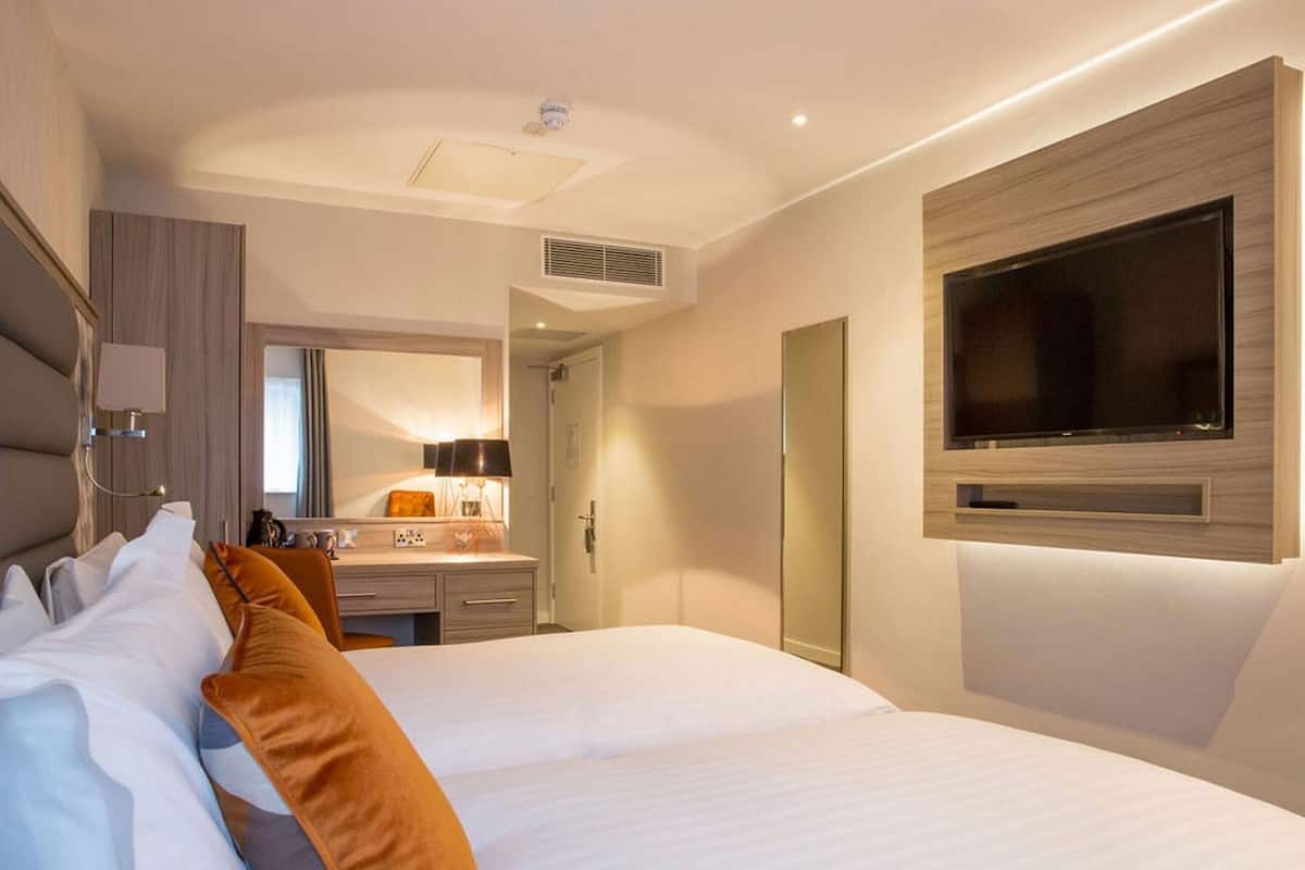 Una habitación de hotel con una cama, un televisor montado en la pared, un escritorio con una lámpara y un espejo.