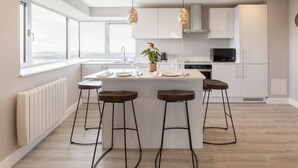 Una cocina moderna con una isla central, taburetes de bar, un microondas y vistas de la ciudad a través de amplios ventanales.