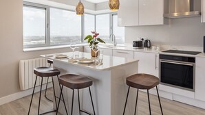 Cocina moderna con una isla grande, taburetes de bar, luces colgantes y vistas a la ciudad.