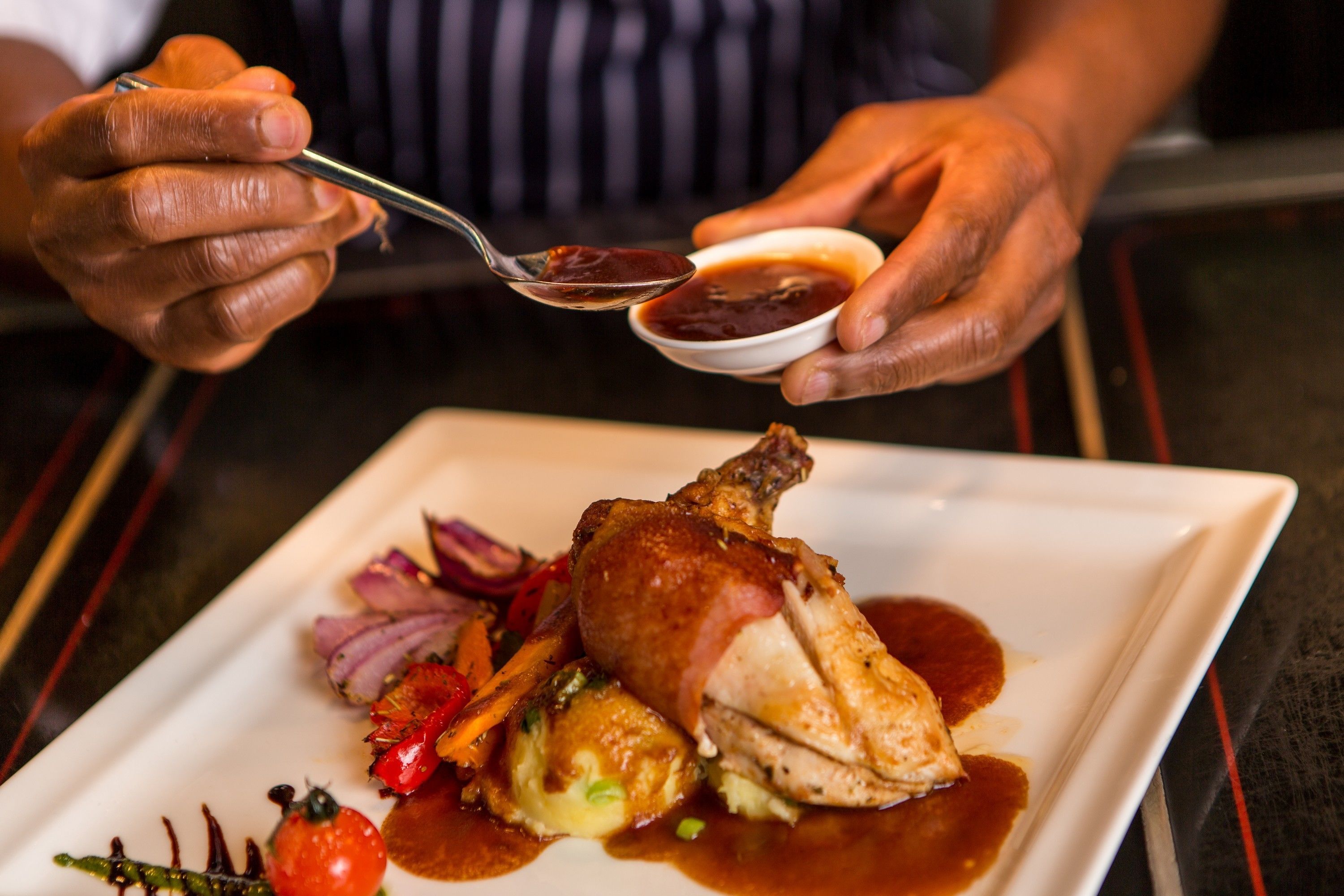 A person holding a spoon with a sauce and a small bowl of sauce.