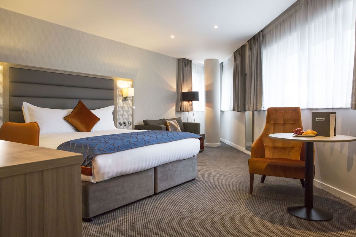 Una habitación de hotel con una cama grande, un escritorio, una silla y una mesita con fruta.