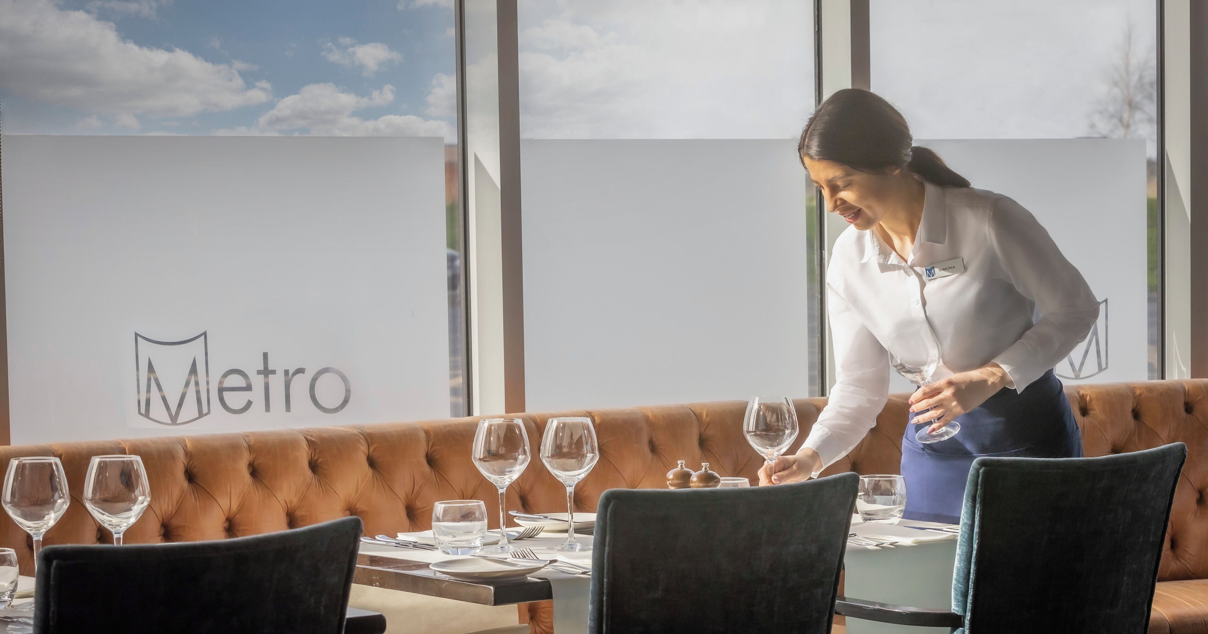 A restaurant setting with a Metro sign in the background, a brown leather booth, and a table set with wine glasses, plates, and cutlery.