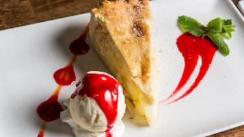 A slice of pie with a dusting of powdered sugar and a red sauce drizzle on a white plate.