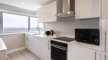 A modern kitchen with white cabinets, a stainless steel range hood, a built-in microwave, and a large window offering a city view.