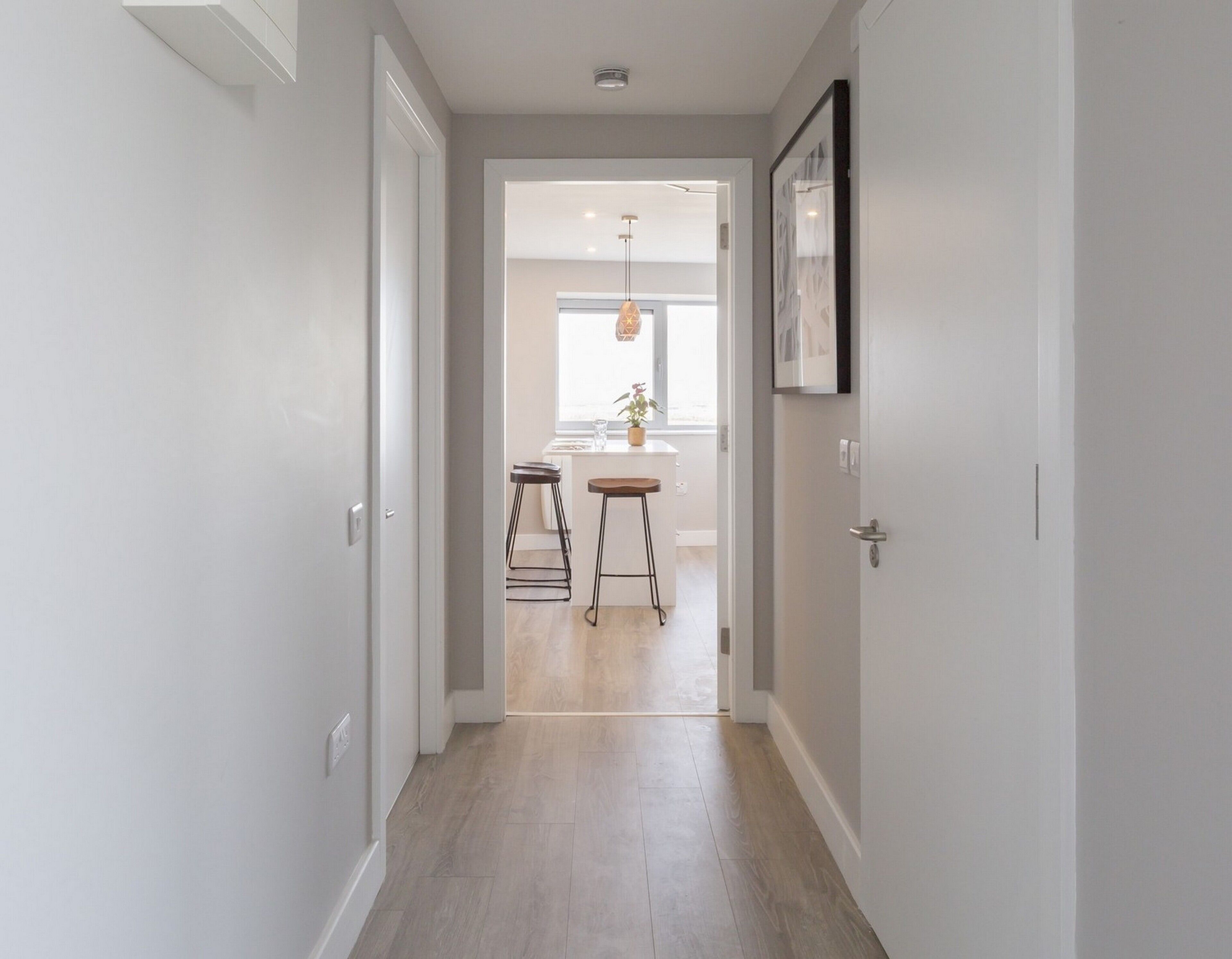 A hallway with a kitchen area in the background, featuring a dining table and stools.