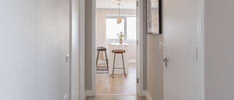 A hallway with a kitchen area in the background, featuring a dining table and stools.