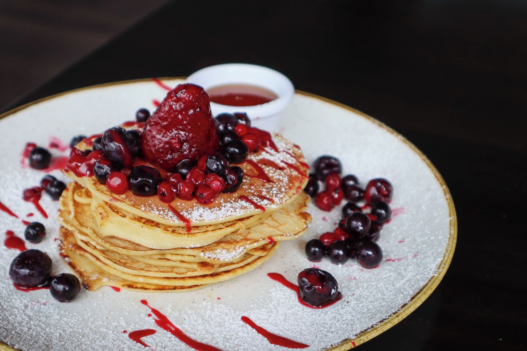 A stack of pancakes topped with berries and a small bowl of syrup.