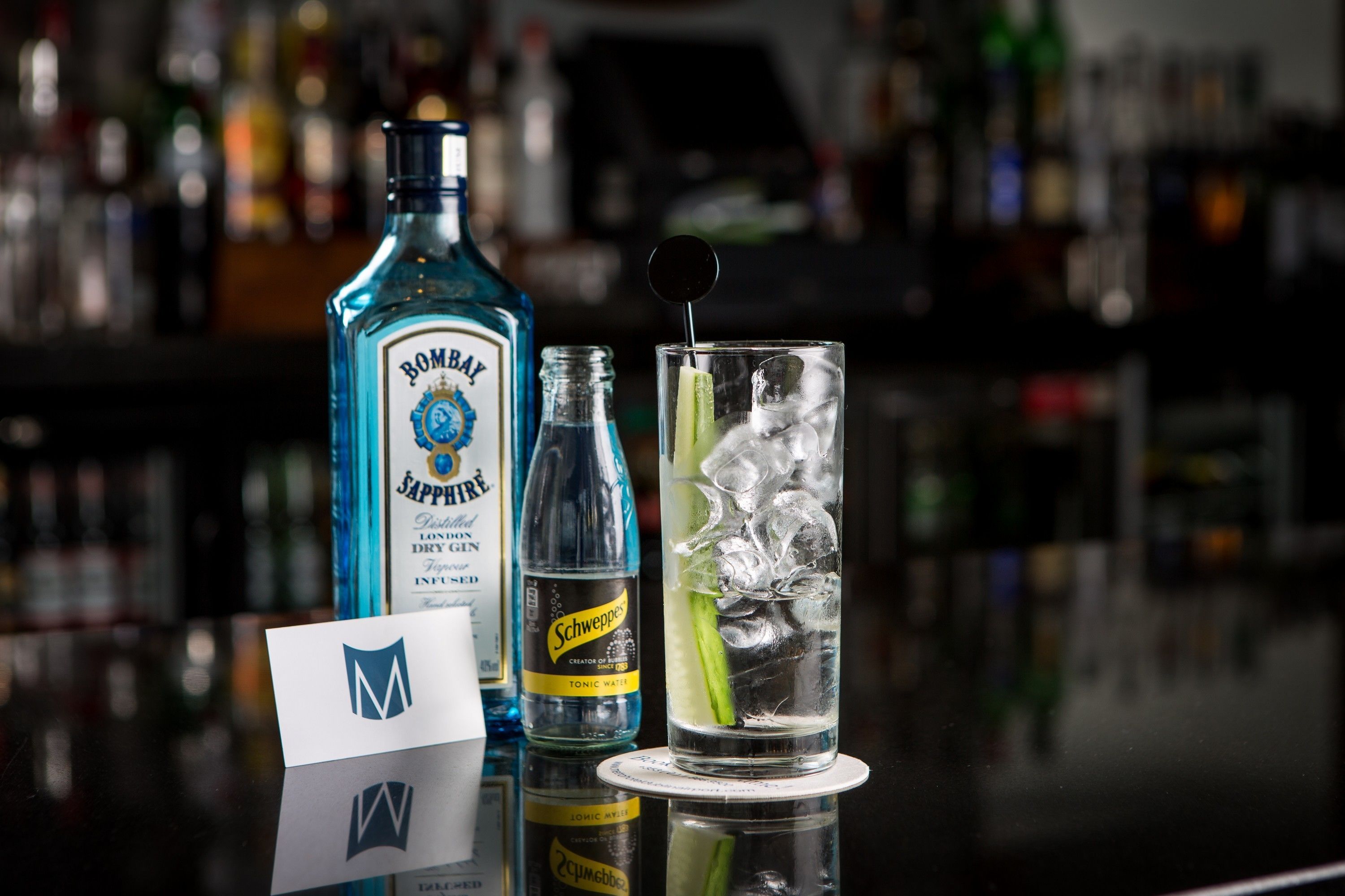 A bar setting with a bottle of Bombay Jaffa, a bottle of Schweppes tonic water, and a glass with ice and a lime slice.