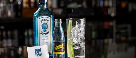 A bar setting with a bottle of Bombay Jaffa, a bottle of Schweppes tonic water, and a glass with ice and a lime slice.
