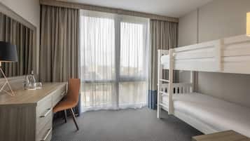 Una habitación de hotel con un escritorio de madera, una silla, una cama nido y un amplio ventanal con cortinas.