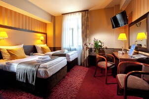 Habitación de hotel con dos camas, un escritorio con computadora, televisor montado en la pared y un espejo.