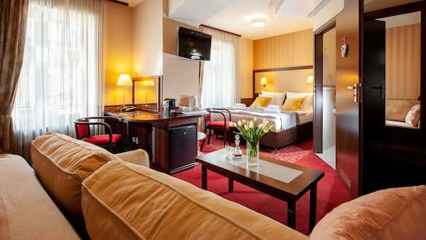 A hotel room with a bed, a desk with a chair, a sofa, a TV, and a red carpet. - Hotel Wielopole (Kraków)