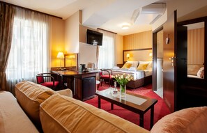 Une chambre d’hôtel avec un lit, un bureau et une chaise, un canapé, une télévision et une moquette rouge.