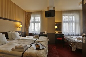 Quarto de hotel com duas camas, uma escrivaninha, uma cadeira, uma televisão e uma janela com cortinas.
