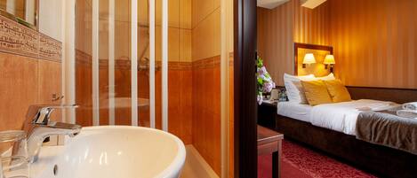 Un baño de hotel con un lavamanos grande, una ducha y una cama con alfombra roja.