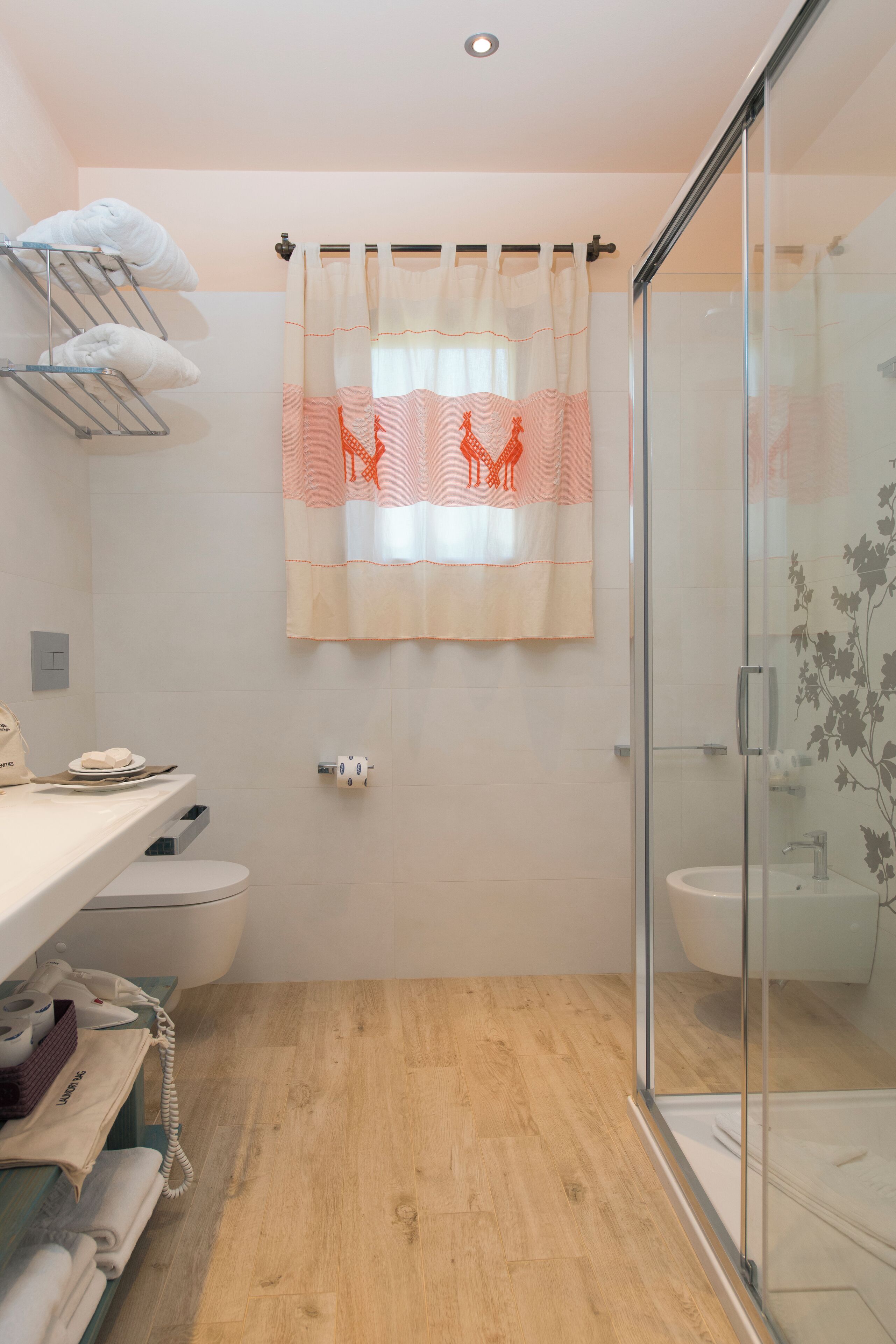 A bathroom with a shower, toilet, and sink. There is a towel rack with towels, a glass shower enclosure, and a curtain with a giraffe design.