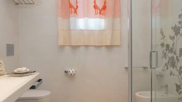 A bathroom with a shower, toilet, and sink. There is a towel rack with towels, a glass shower enclosure, and a curtain with a giraffe design.