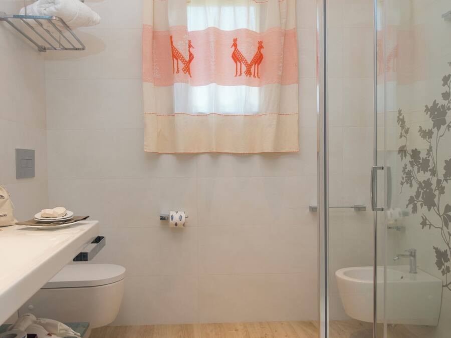 A bathroom with a shower, toilet, and sink. There is a towel rack with towels, a glass shower enclosure, and a curtain with a giraffe design.