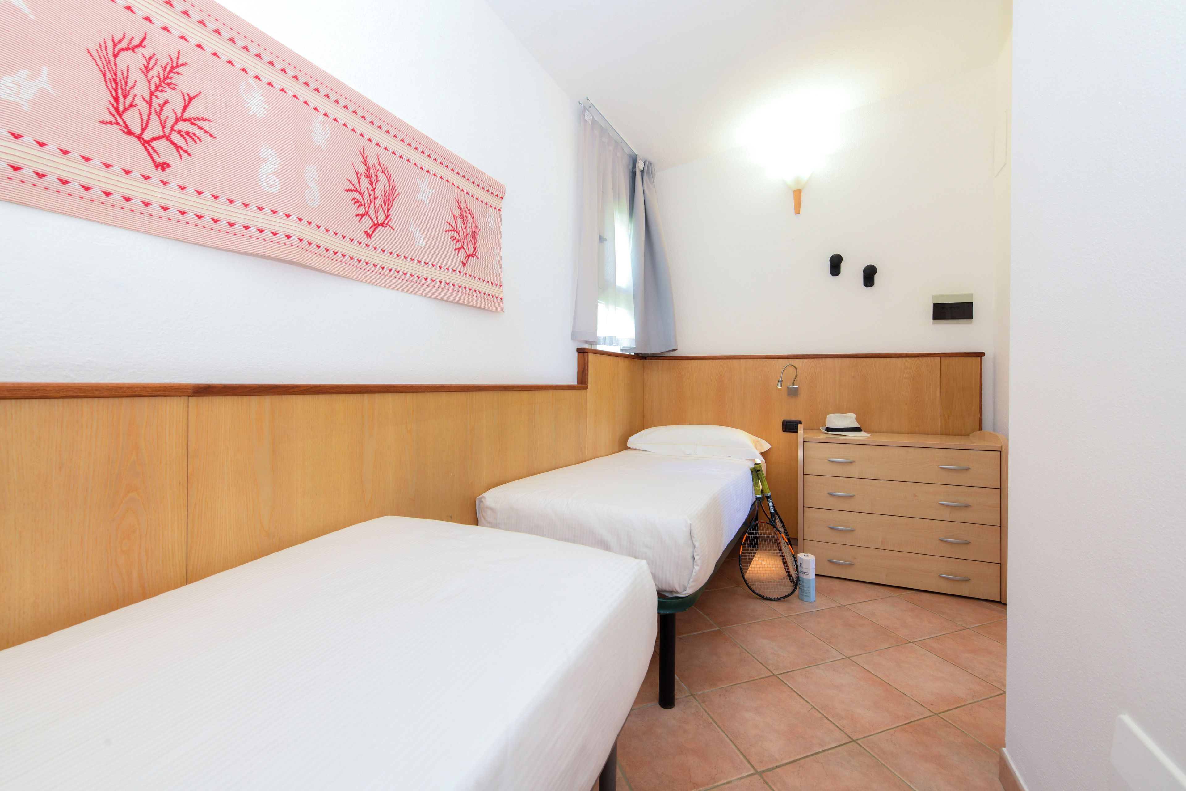 Een hotelkamer met twee eenpersoonsbedden, een houten dressoir en een wandlamp.
