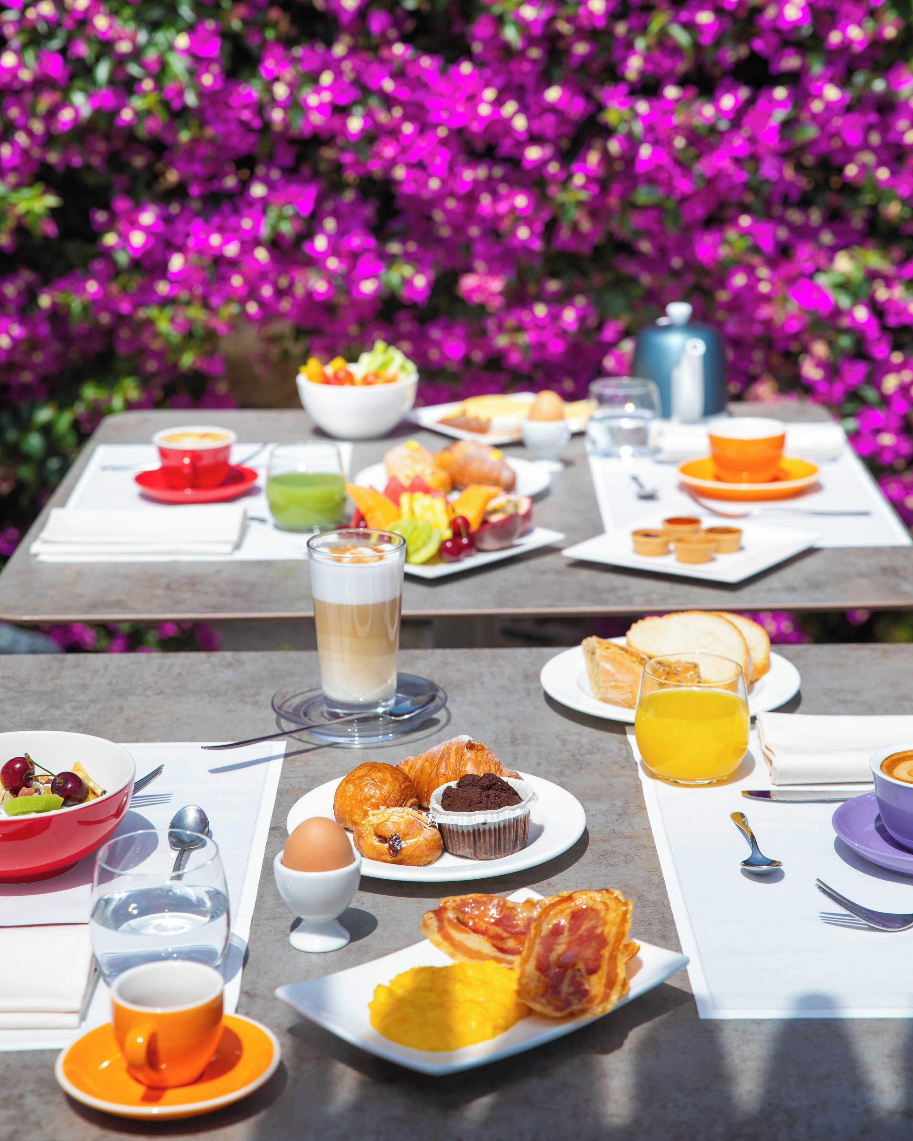 A table set with breakfast items including croissants, muffins, and fruit, with a vibrant purple flower background.