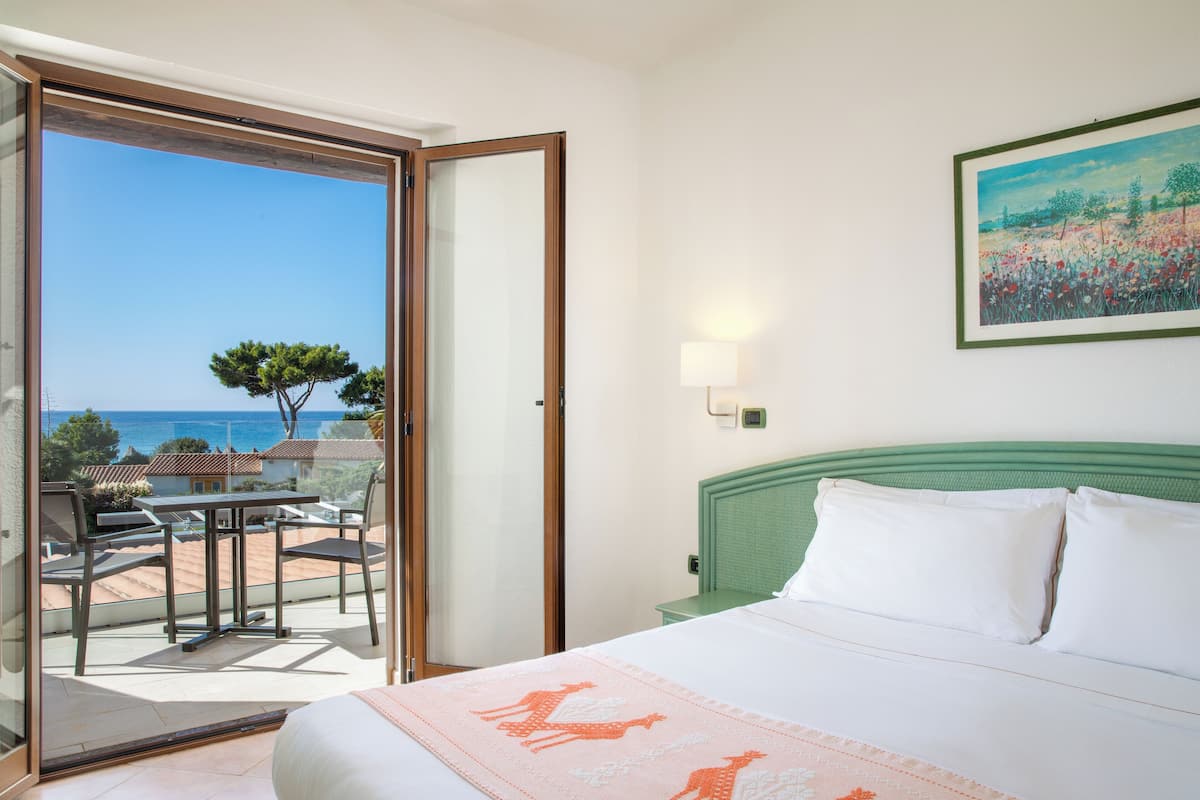 A hotel room with a bed, a balcony with a table and chairs, and a painting on the wall.