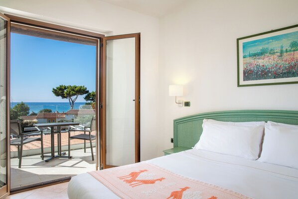 A hotel room with a bed, a balcony with a table and chairs, and a painting on the wall. - Cormoran Resort Villasimius (Villasimius)