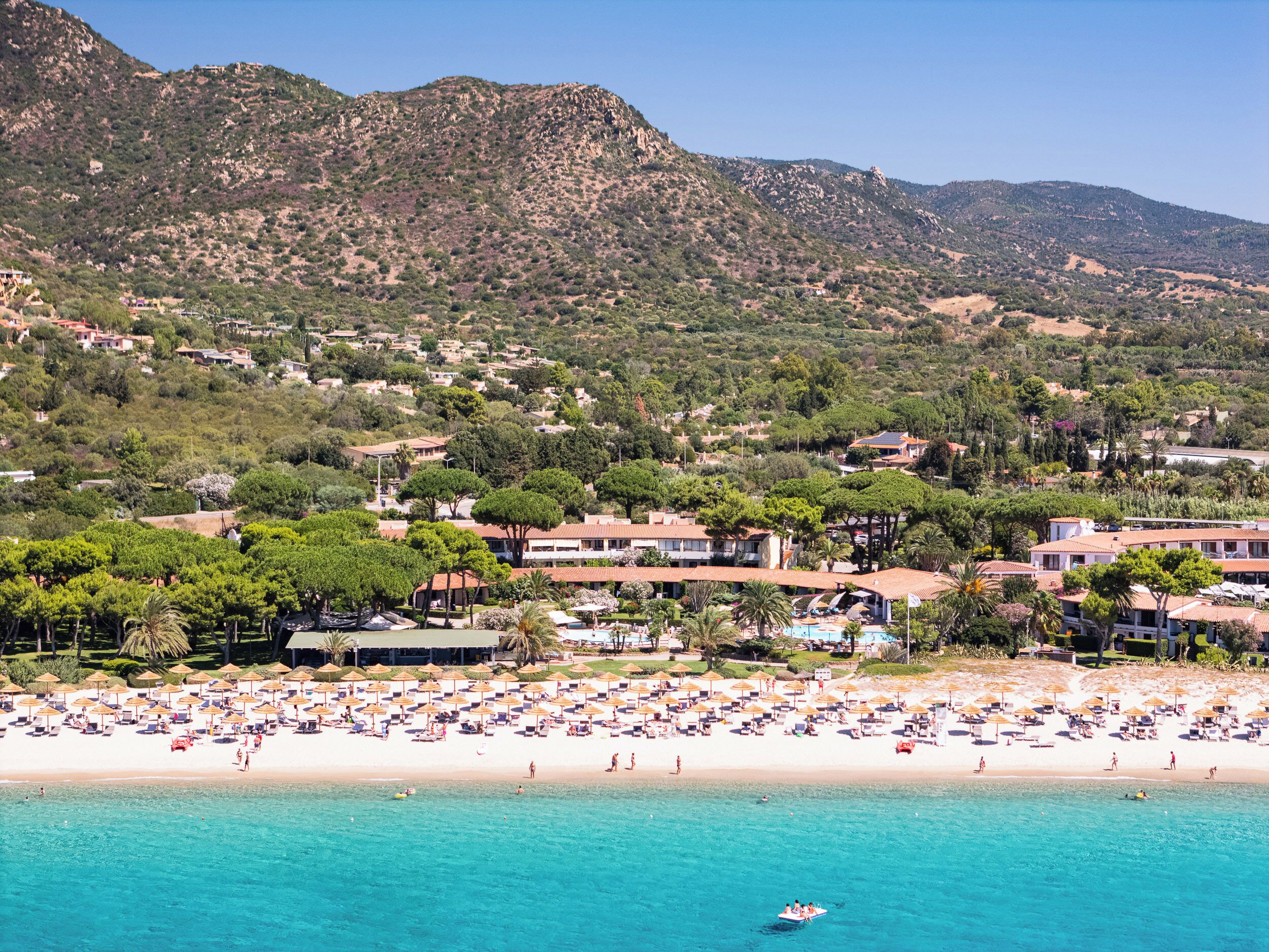 A coastal resort with a beach, villas, and a mountainous backdrop.