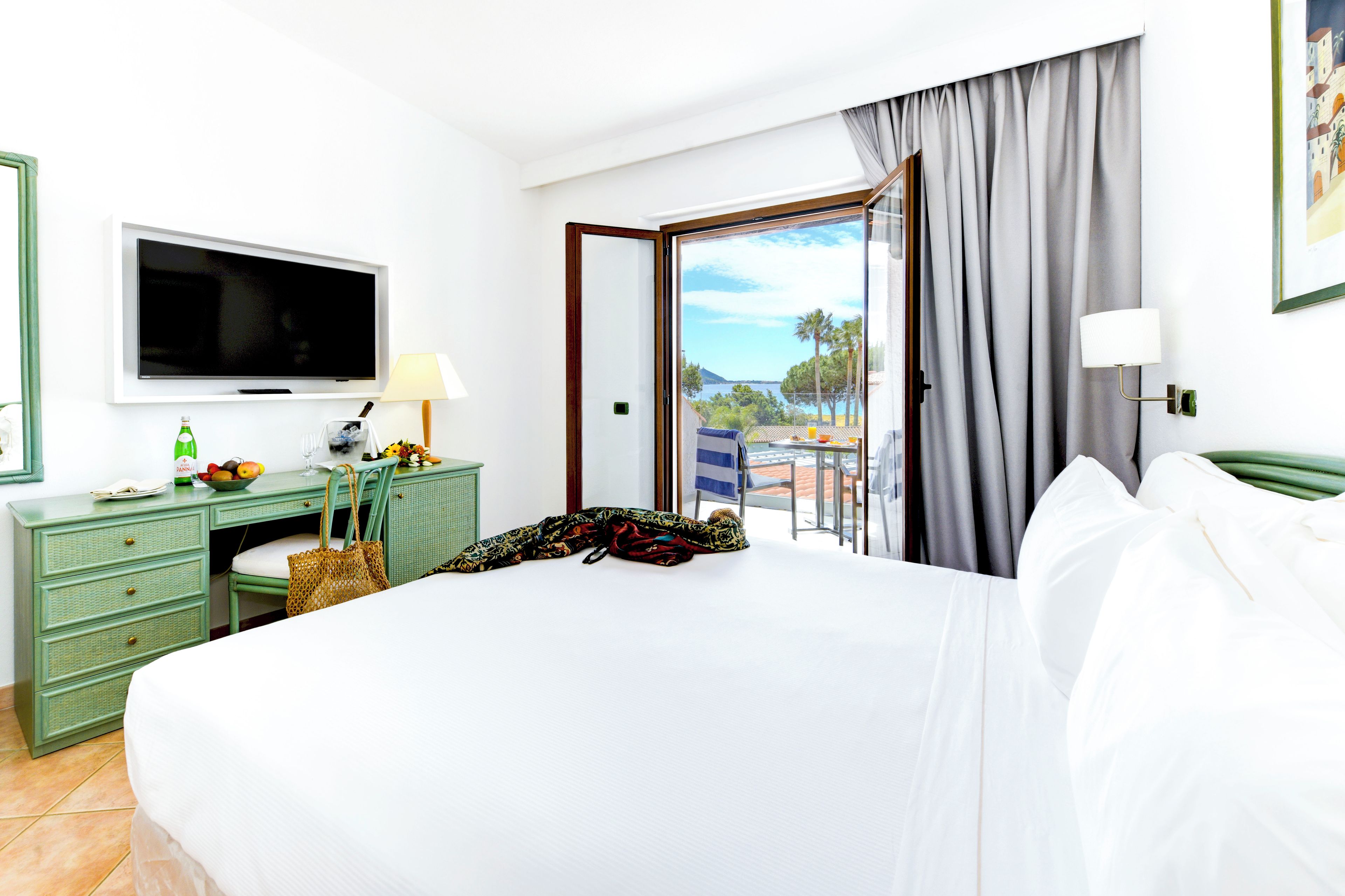 Habitación de hotel con una cama, un escritorio con televisor, una lámpara y vista al mar.