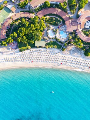 Vista aérea de un complejo turístico con playa, piscina y cancha de tenis.