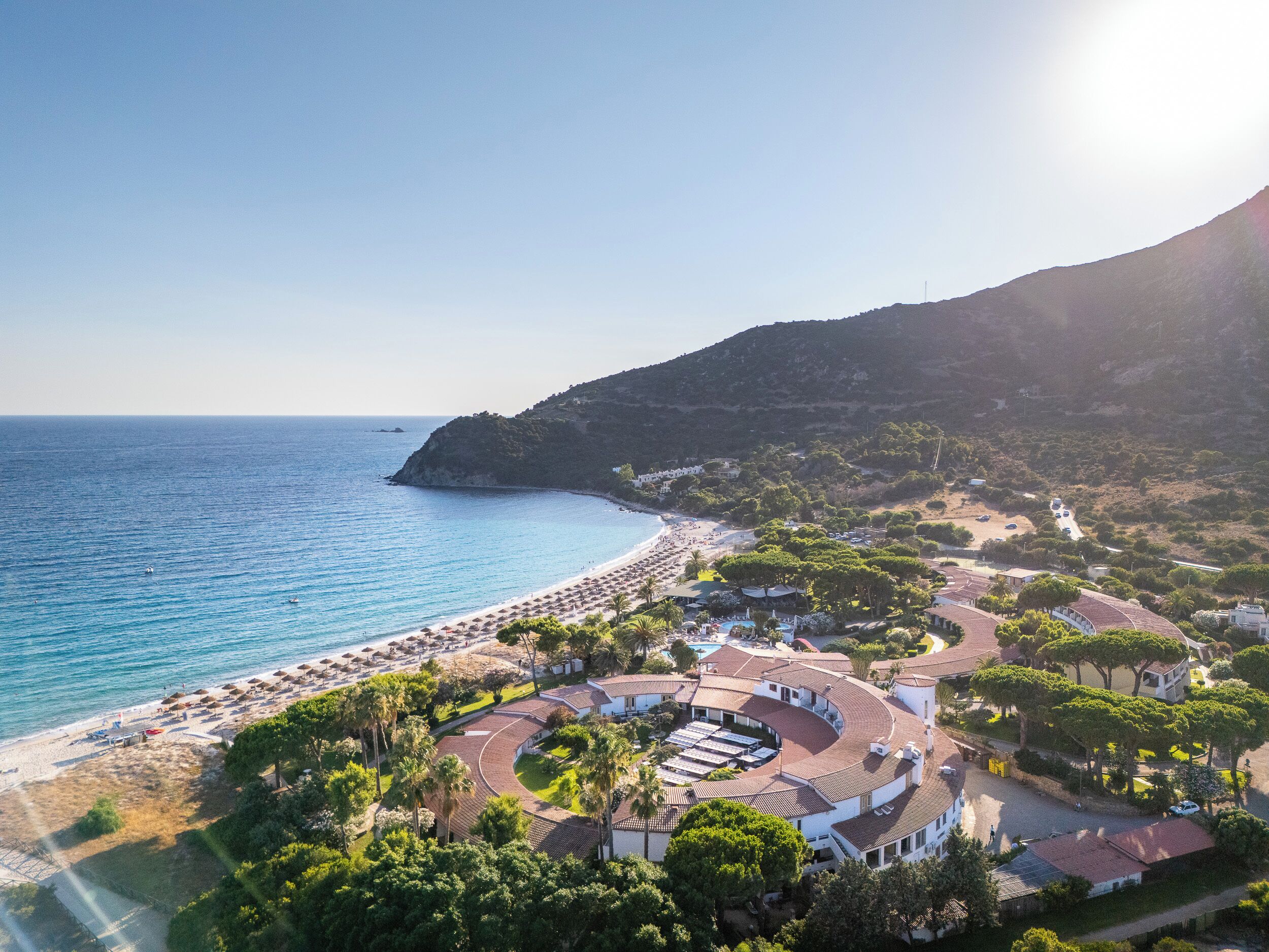 An aerial view of a coastal resort with a beach, villas, and a pool area.