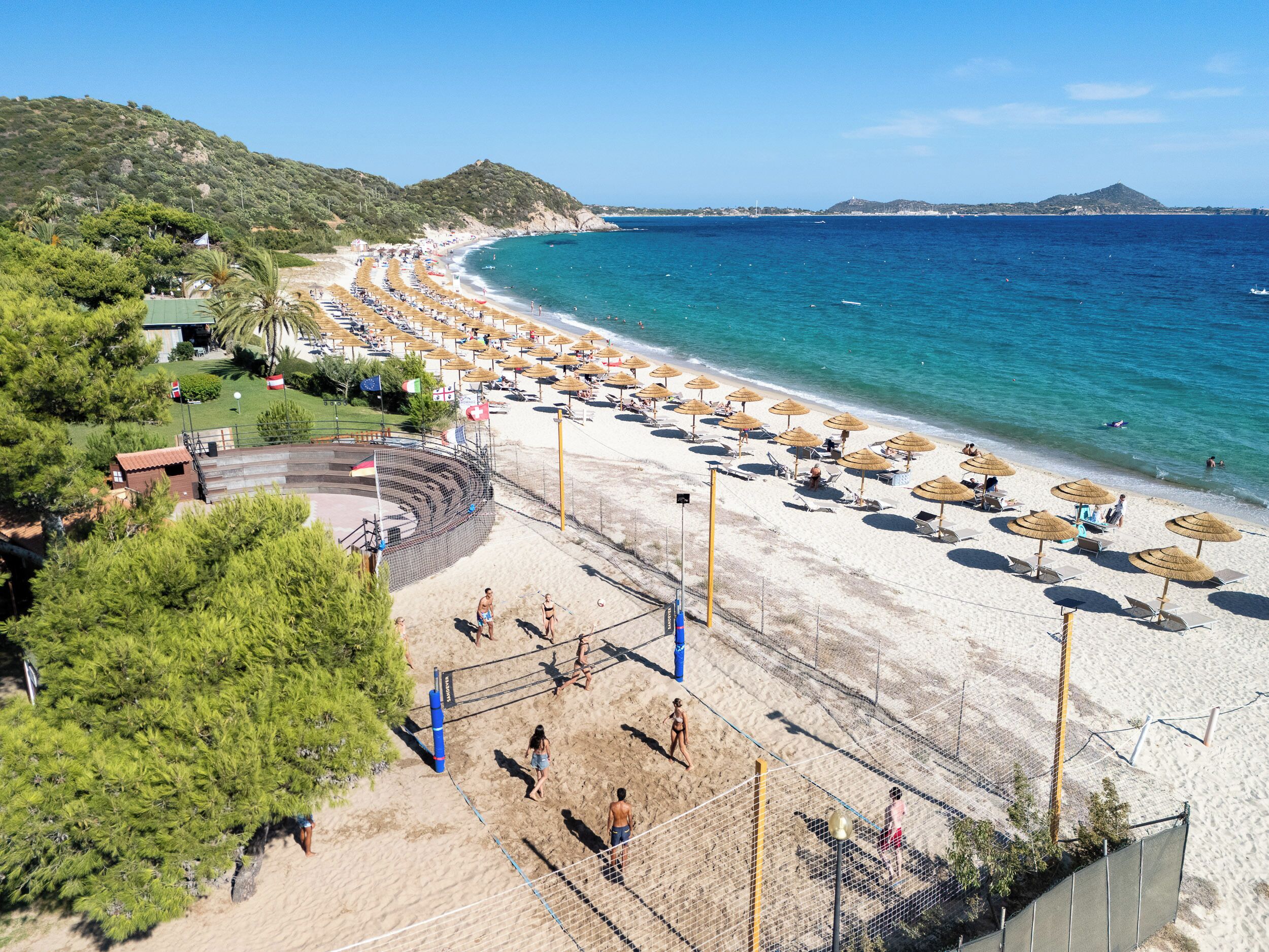 A beach with a volleyball net, umbrellas, and beach chairs.
