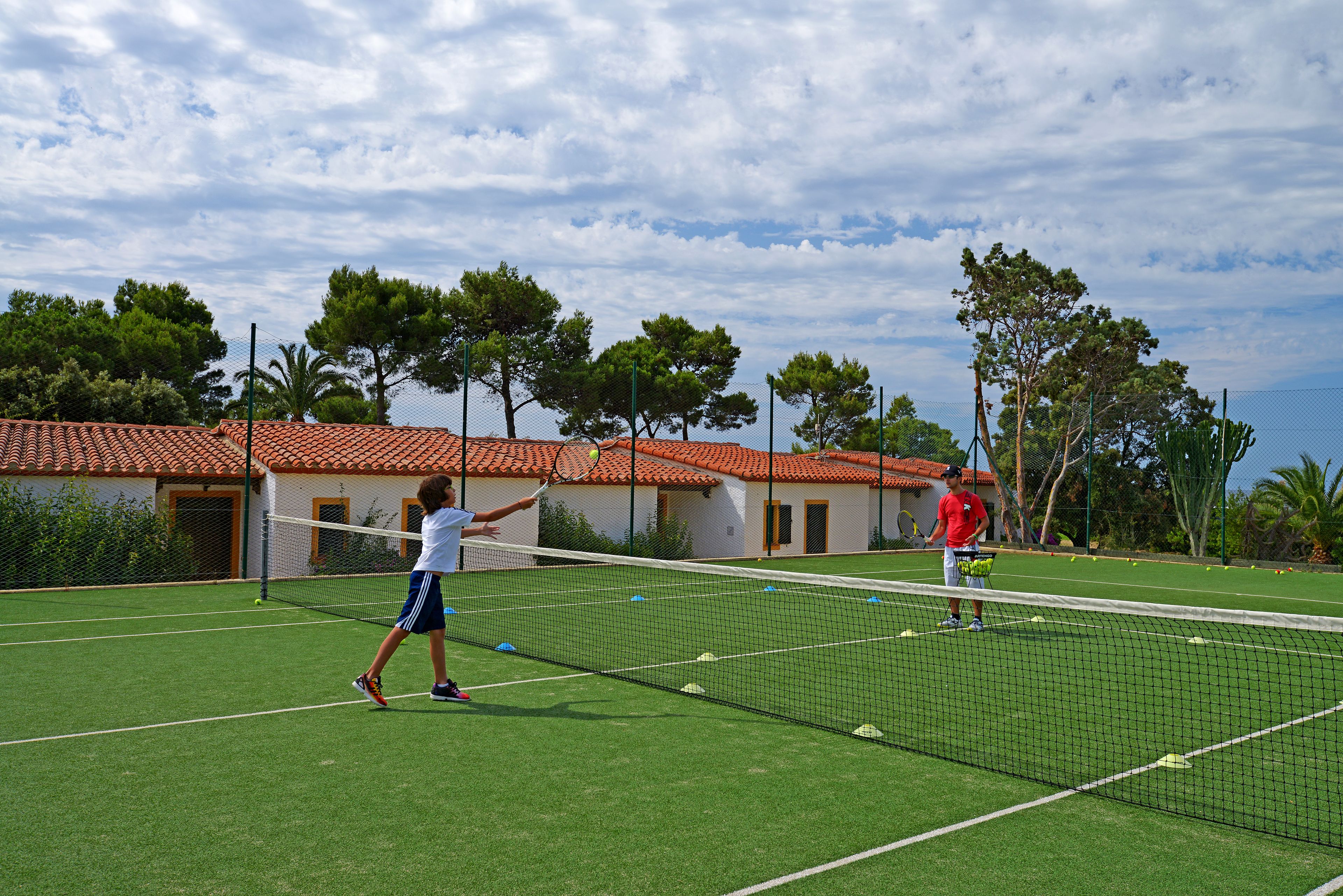 A tennis court with a net, surrounded by a fence and trees.