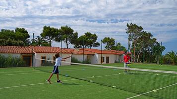A tennis court with a net, surrounded by a fence and trees.